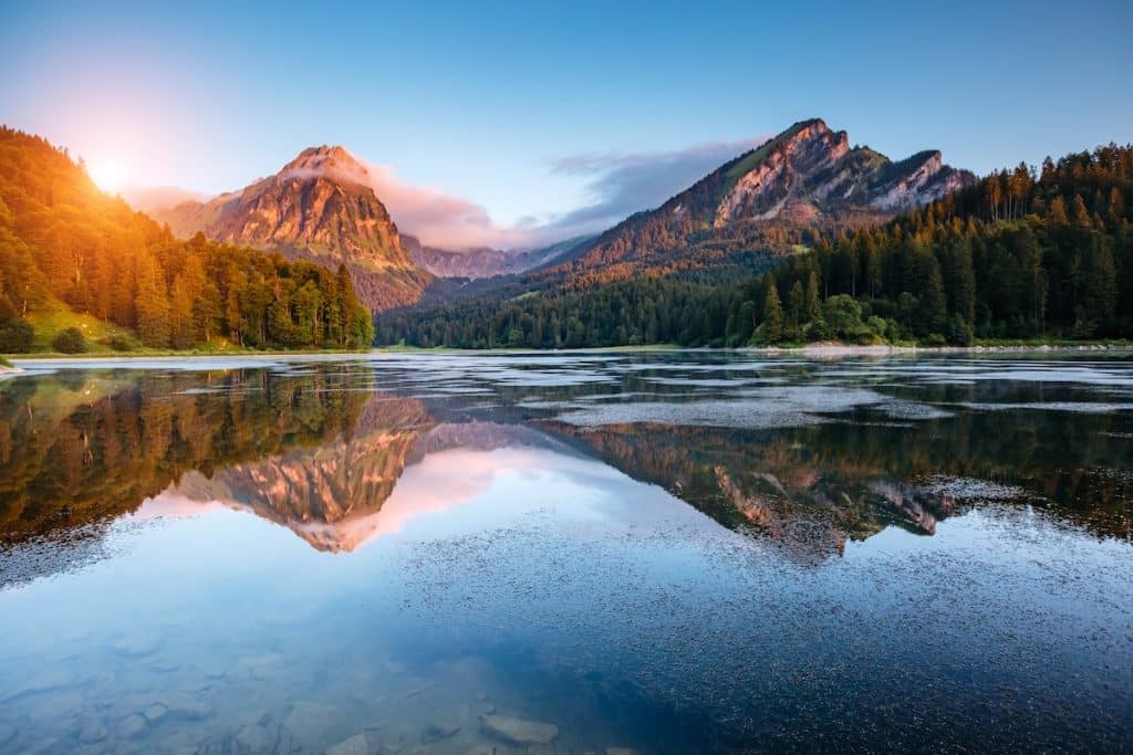 Lac alpin au coucher de soleil avec reflets dorés des montagnes et forêts - photographie de paysage de montagne en heure dorée